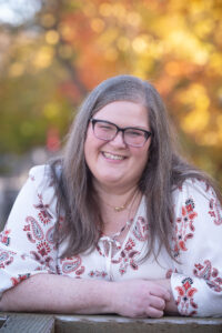 Susan, a middle aged fat woman smiles with fall leaves behind her